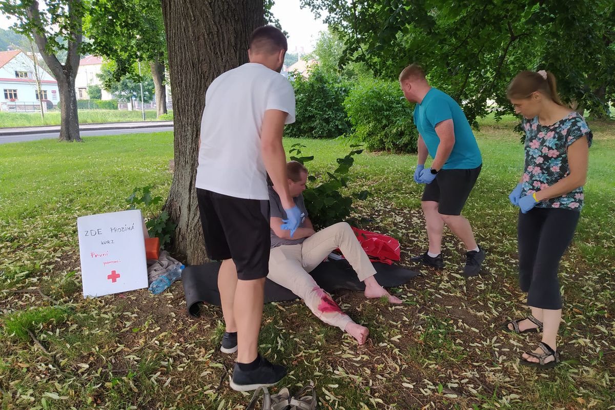 Účastníci kurzu ošetřují zraněného při simulaci venku pod stromem